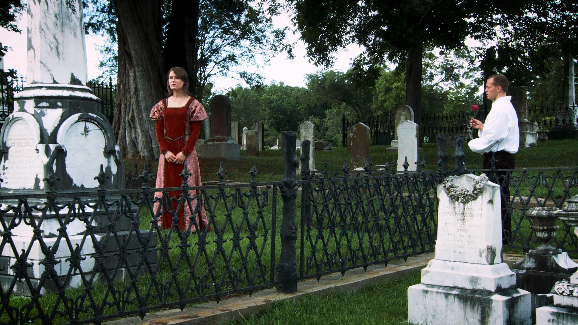 A man offering a rose to a woman in red among the gravestones